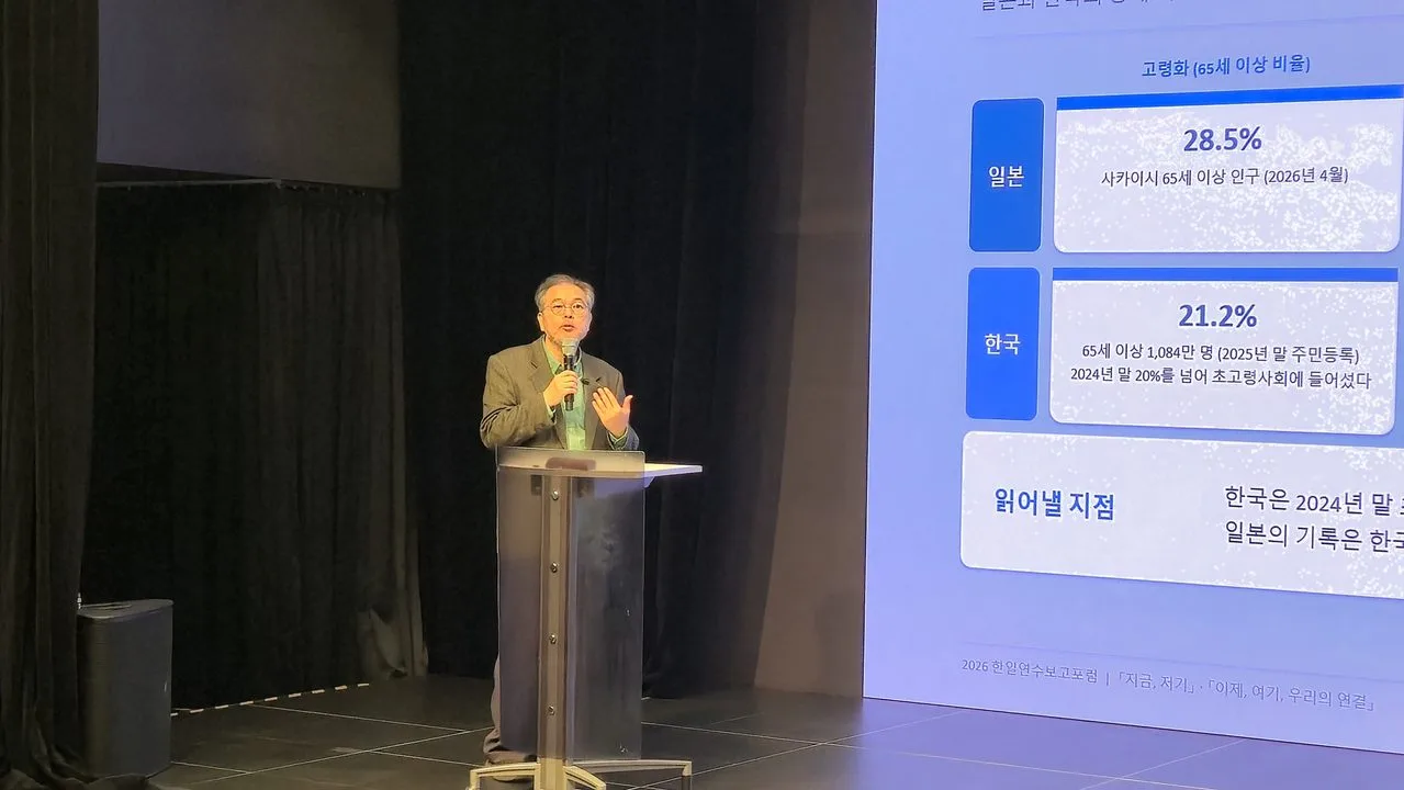 한일 연수 보고 포럼 무대에서 연구공방의 강내영 수석연구위원이 마이크를 들고 발제하는 모습. 오른쪽 화면에는 한국과 일본의 고령화 비율을 비교한 발표 자료가 보인다.