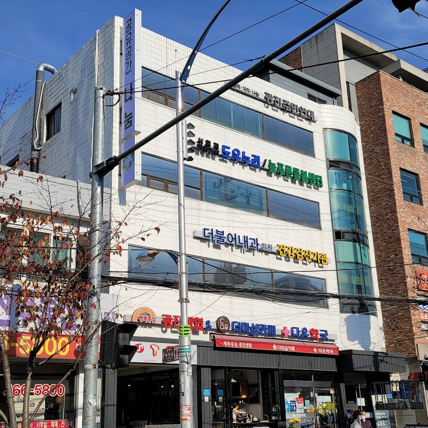 모퉁이에서 올려다본 공유공간 나눔 건물. 1층 광진생협·더마실카페·다온약국, 위층에 광진주민연대와 도우누리 간판이 보인다